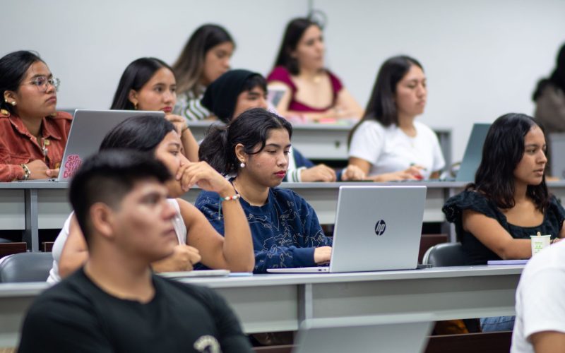 Estudiante concentrado frente a un ordenador portátil en una biblioteca iluminada.